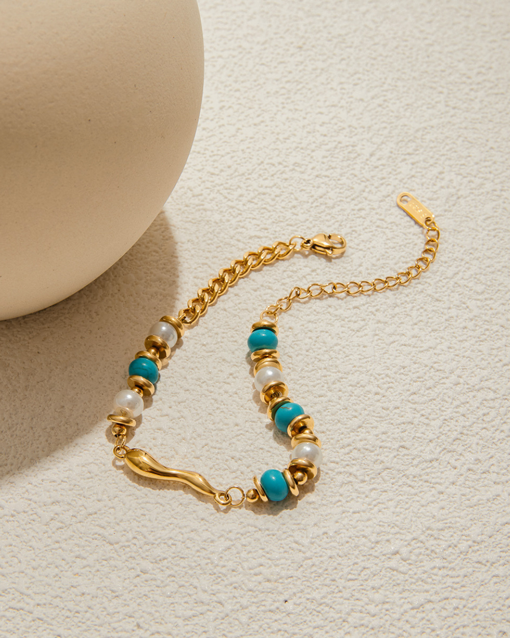 Gold bracelet with turquoise and pearl beads on a beige background