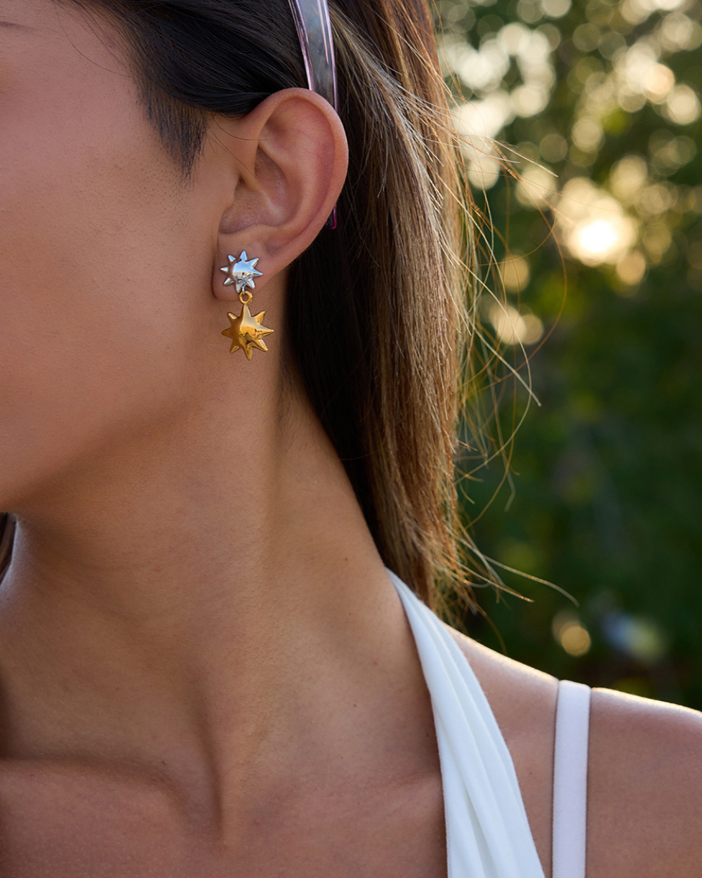 Close-up of a person wearing sun-shaped earrings with a blurred natural background