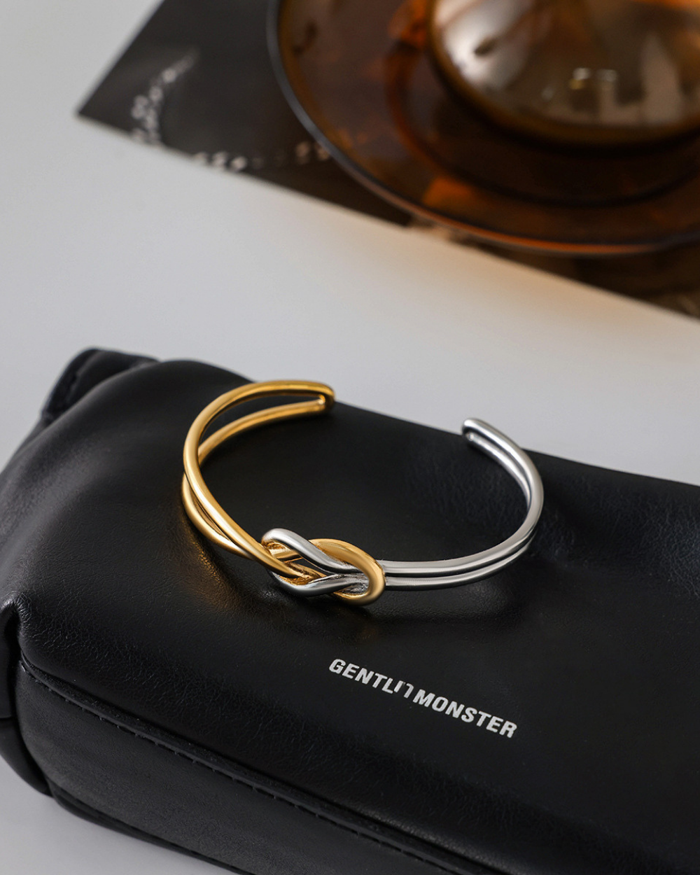 Gold and silver bracelet on a black Gentle Monster case with a blurred background
