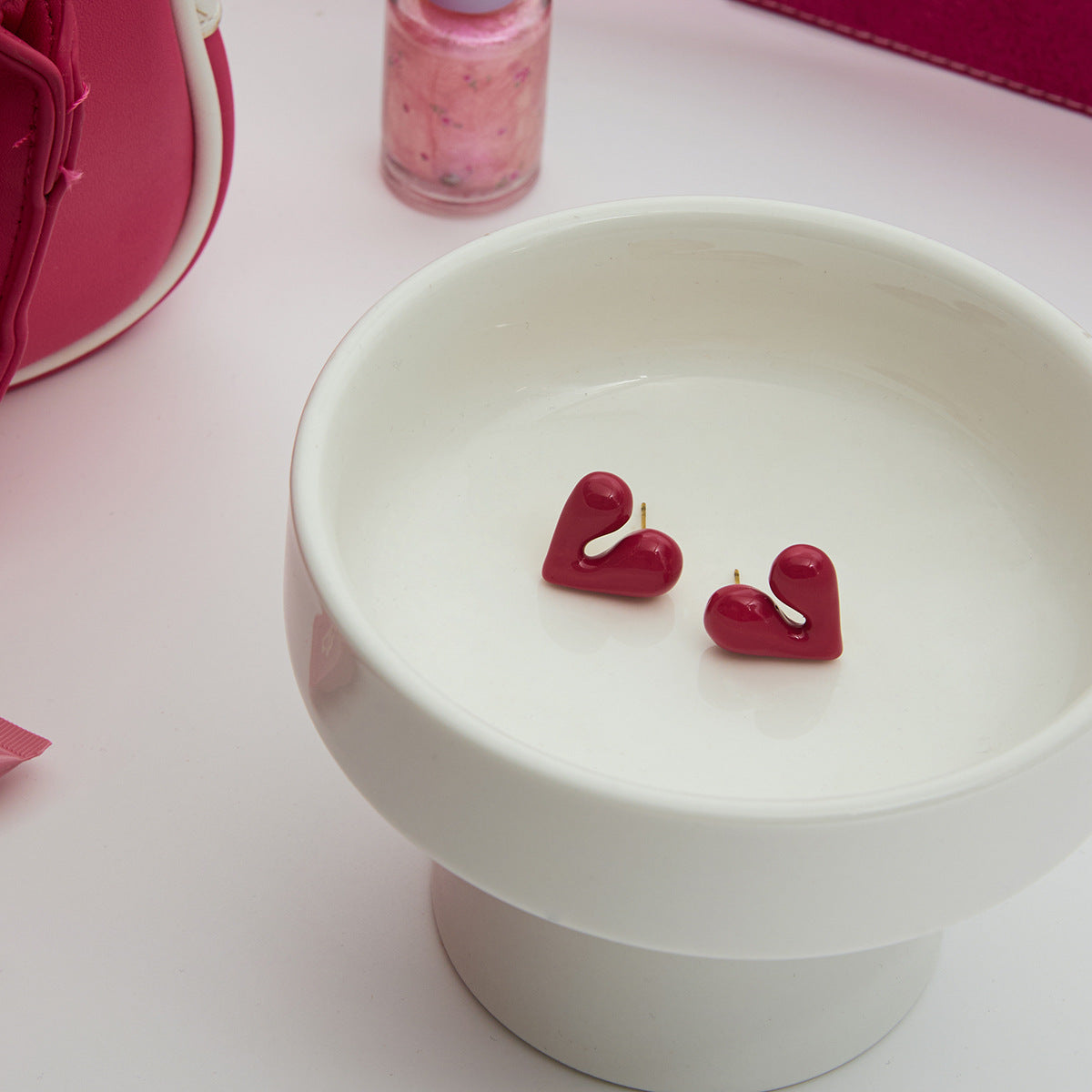 Pink heart earrings displayed in a white ceramic dish