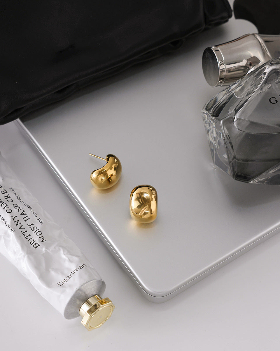 Gold earrings on a white surface with a perfume bottle and skincare product.