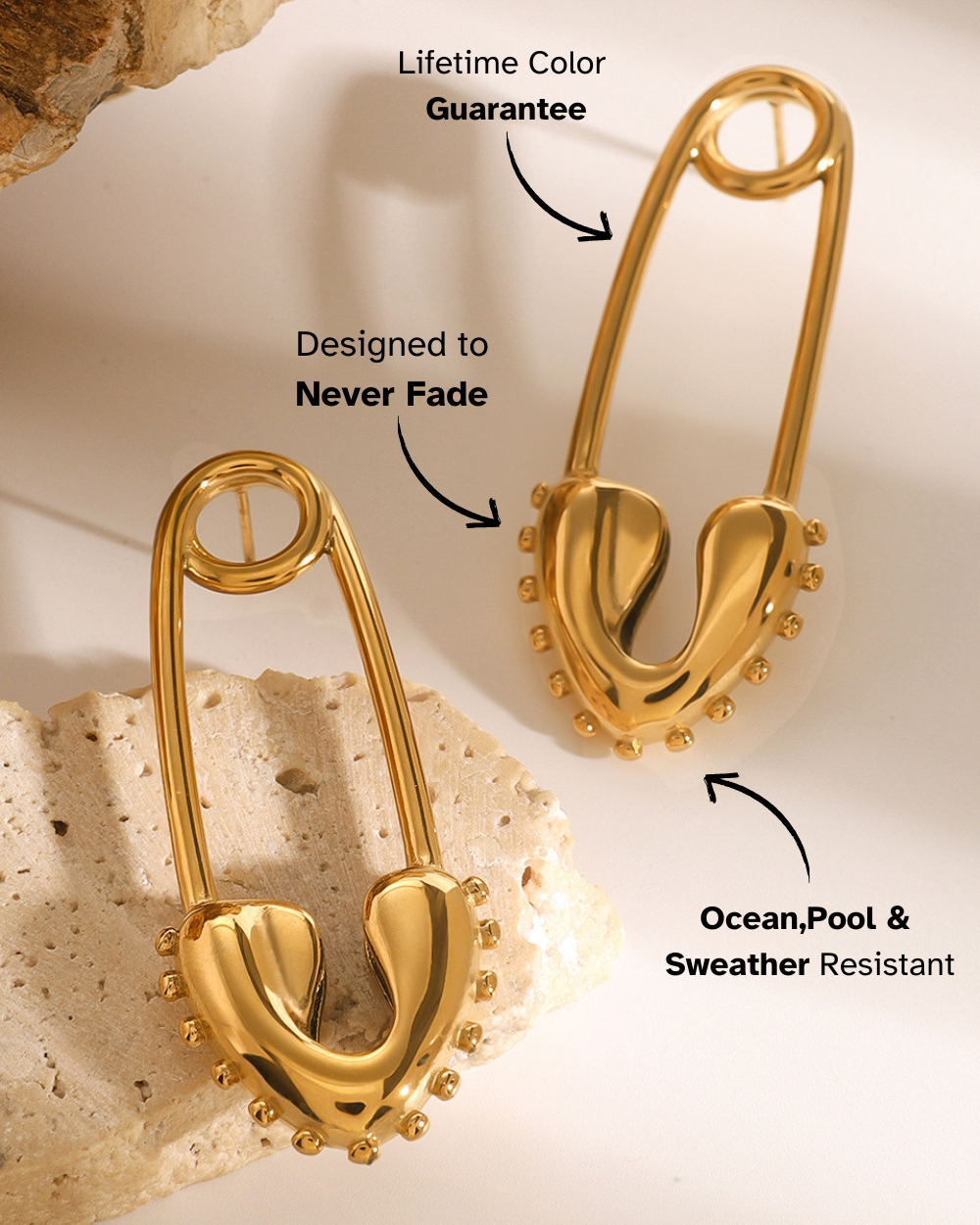 Gold safety pin earrings on a textured beige background with text about color guarantee and resistance.