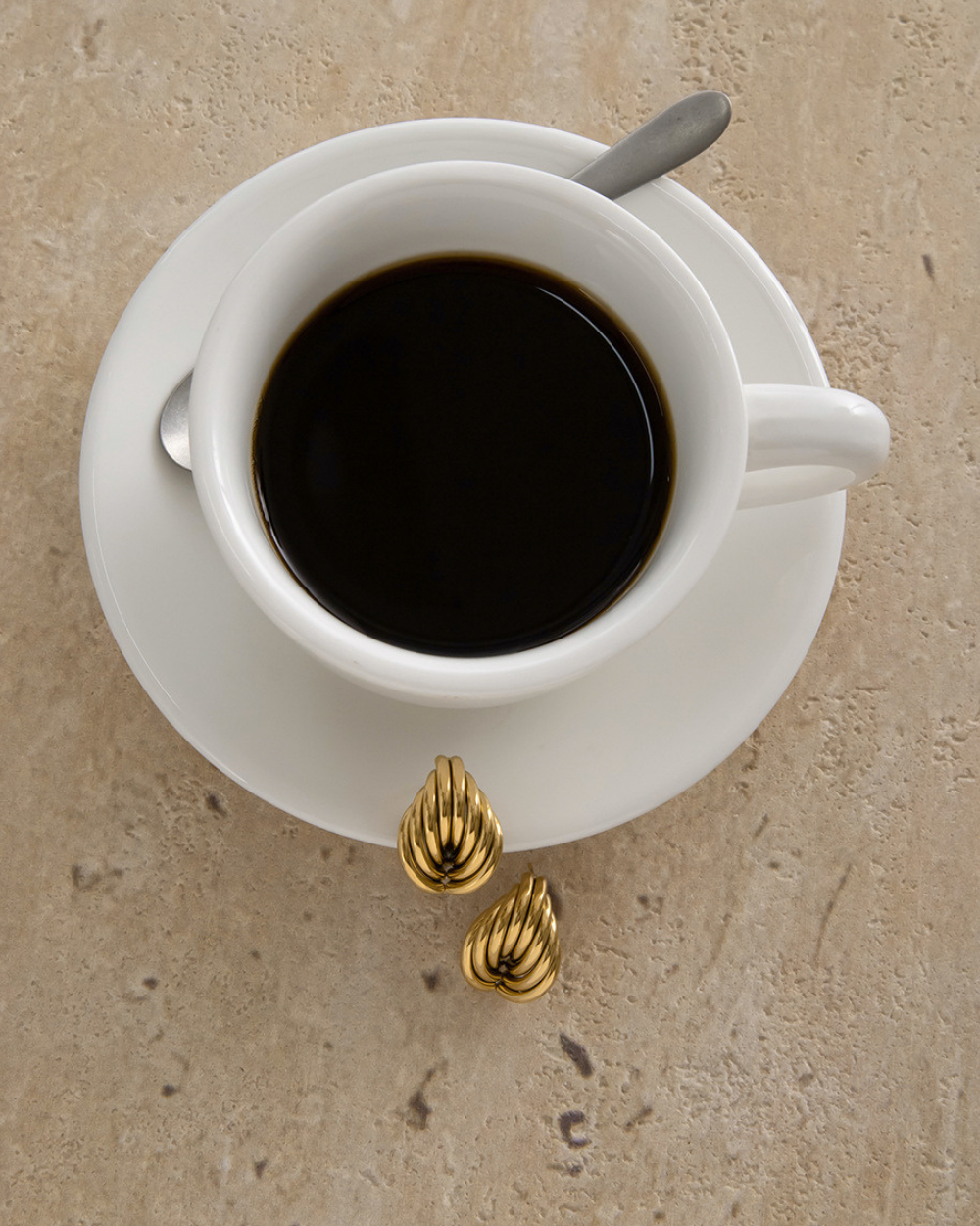 White cup of coffee on a beige surface with gold decorative elements.