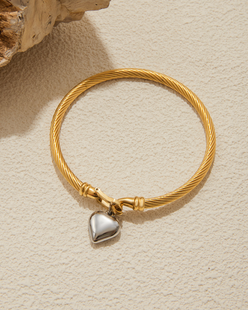 Gold bracelet with a heart-shaped charm on a beige surface