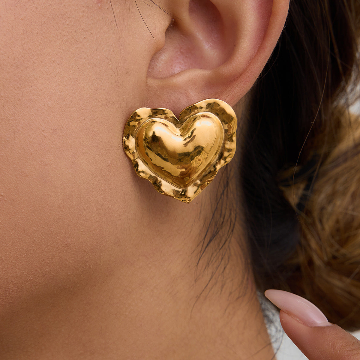 Woman wearing bold gold heart earrings styled with nude manicure
