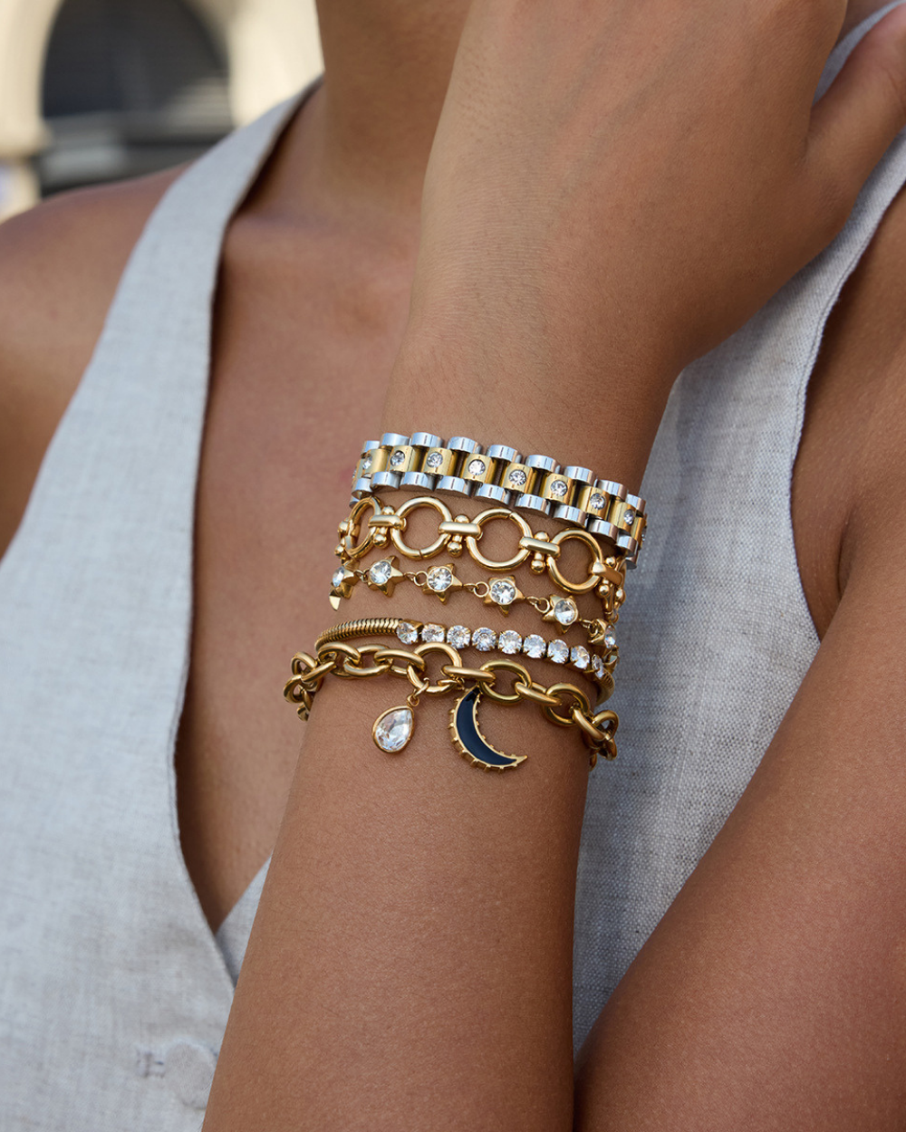 Stack of gold and silver bracelets on a person's wrist with a neutral background