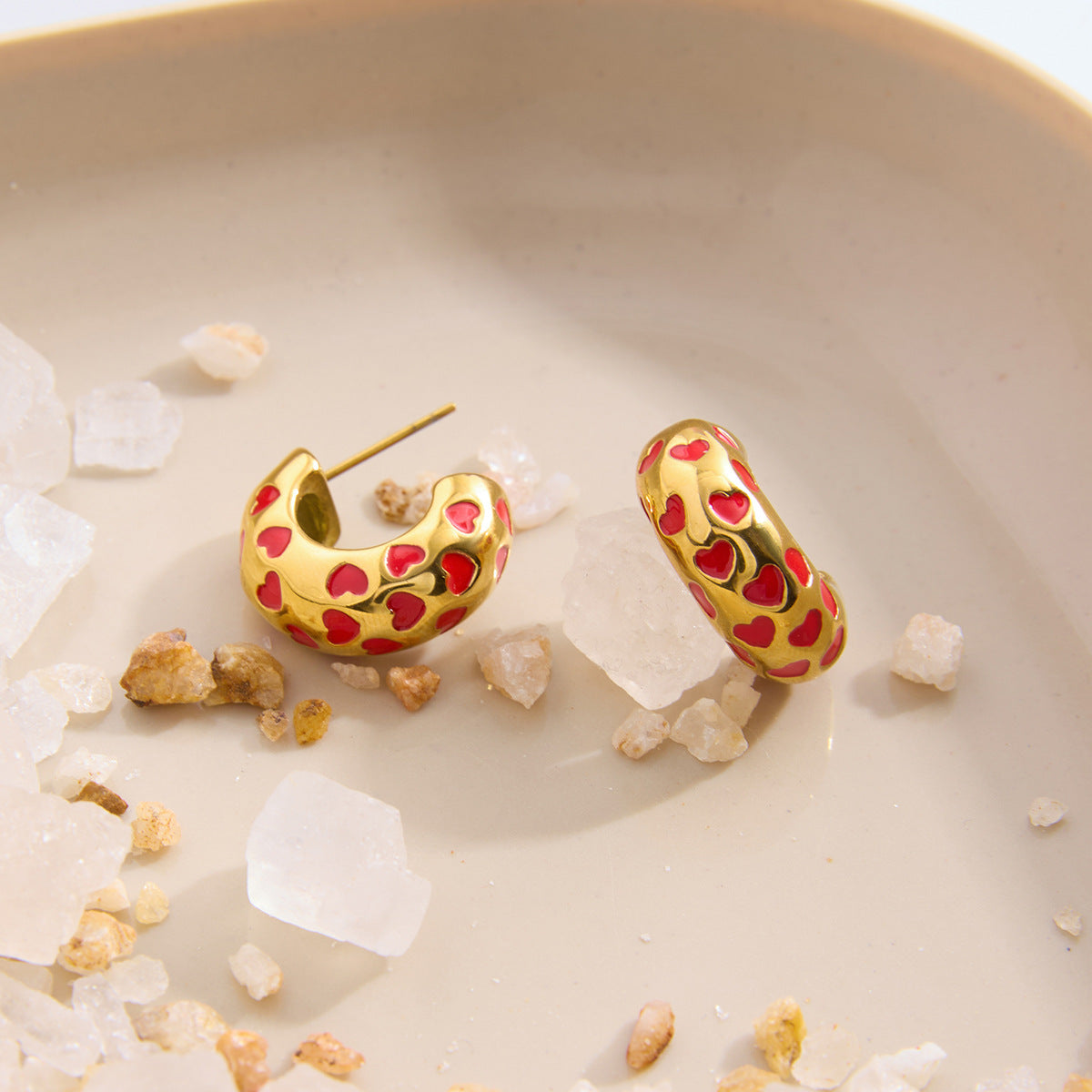 Red heart enamel earrings on white ceramic dish