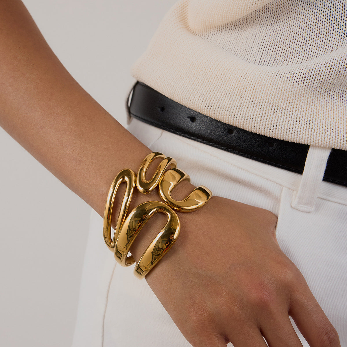 Thick gold sculptural cuff worn with casual white pants and belt