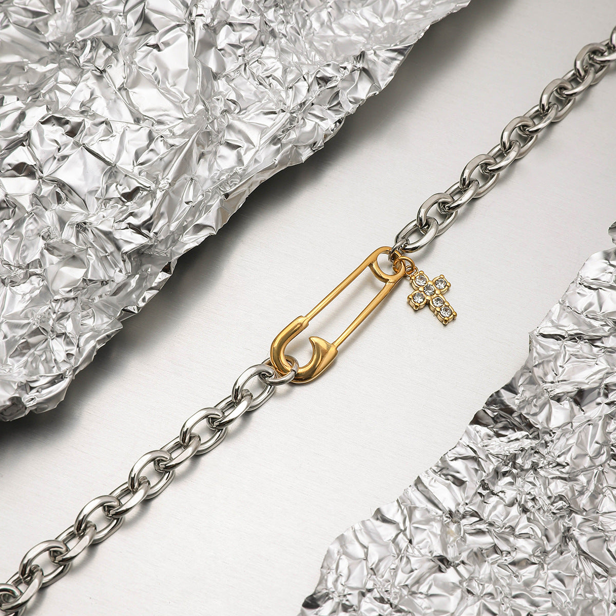 Close-up of model wrist stacking the gold and silver bracelet with rhinestone cross, styled with pastel dress.