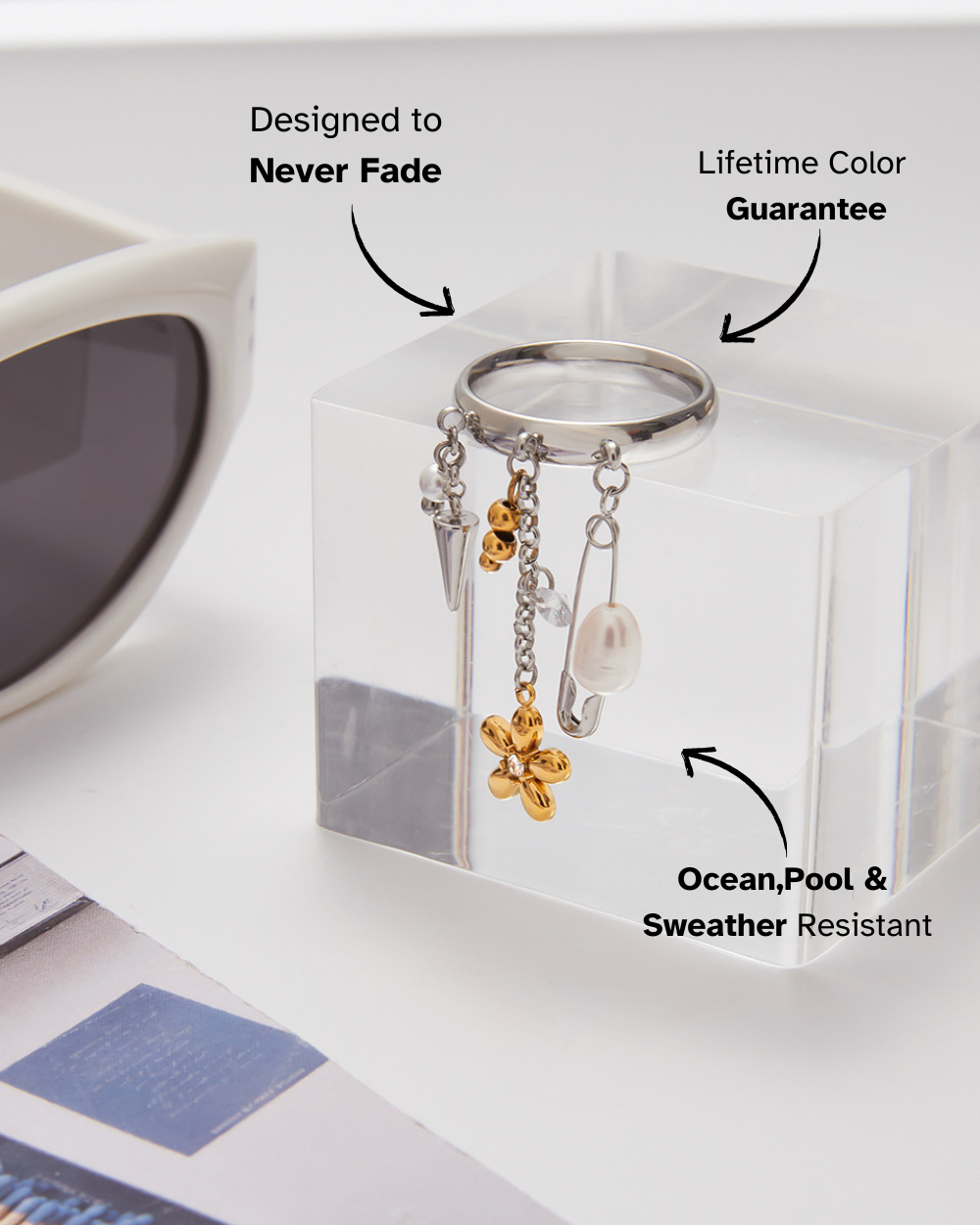 Silver keychain with charms in a clear box, sunglasses in the background