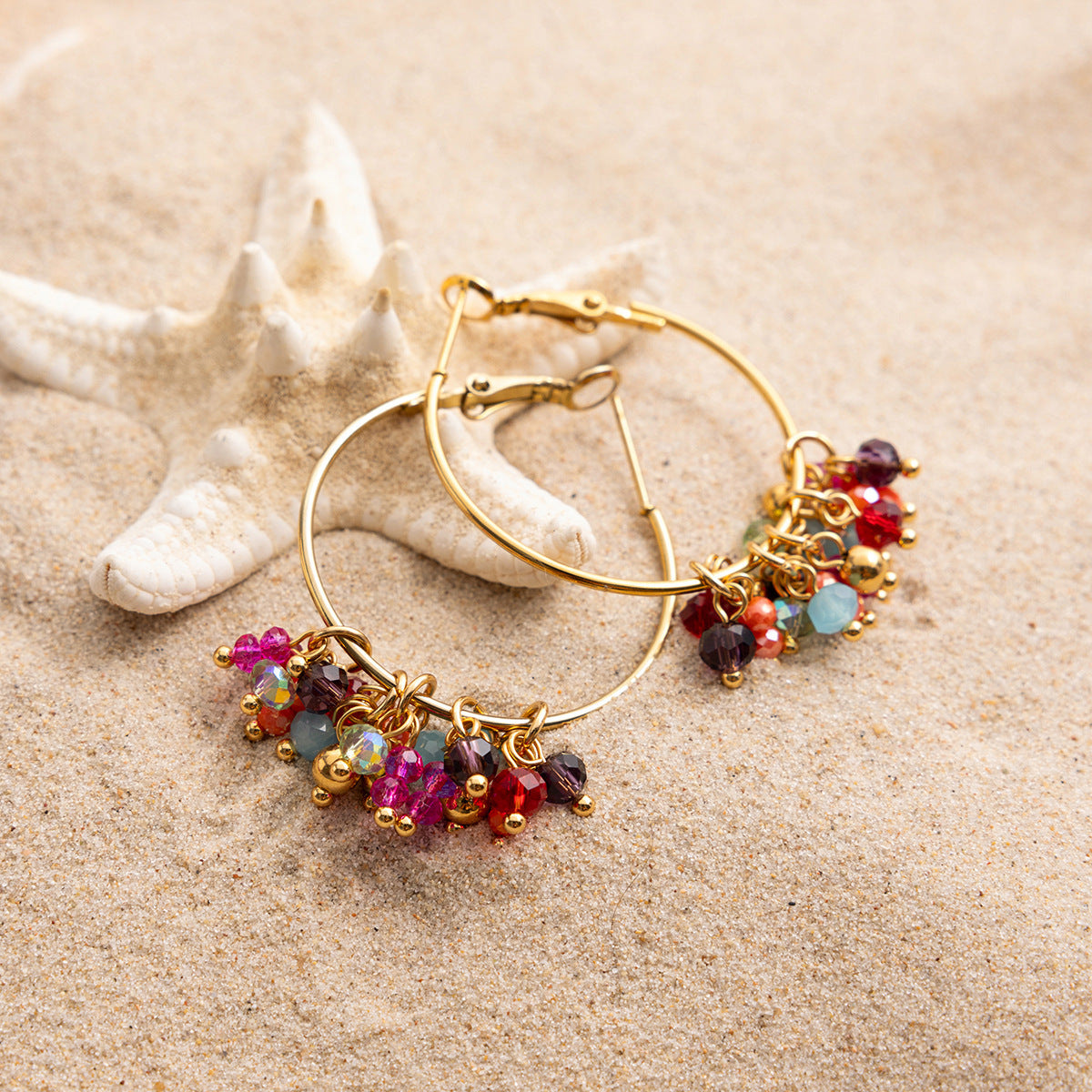 Gold hoop earrings with colorful beads on a sandy background