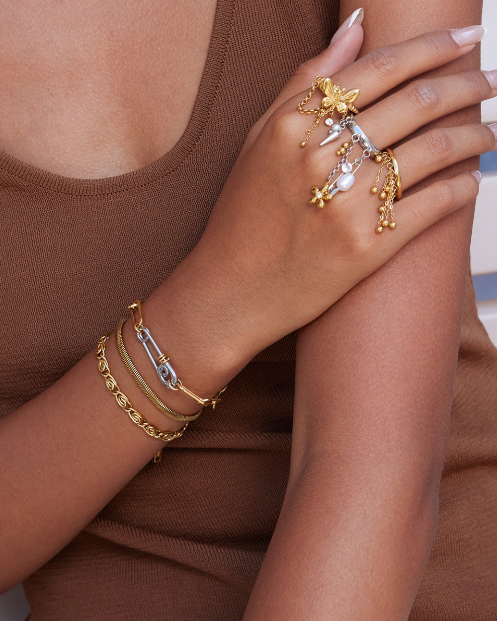 Hand wearing a gold ring and bracelets on a brown background