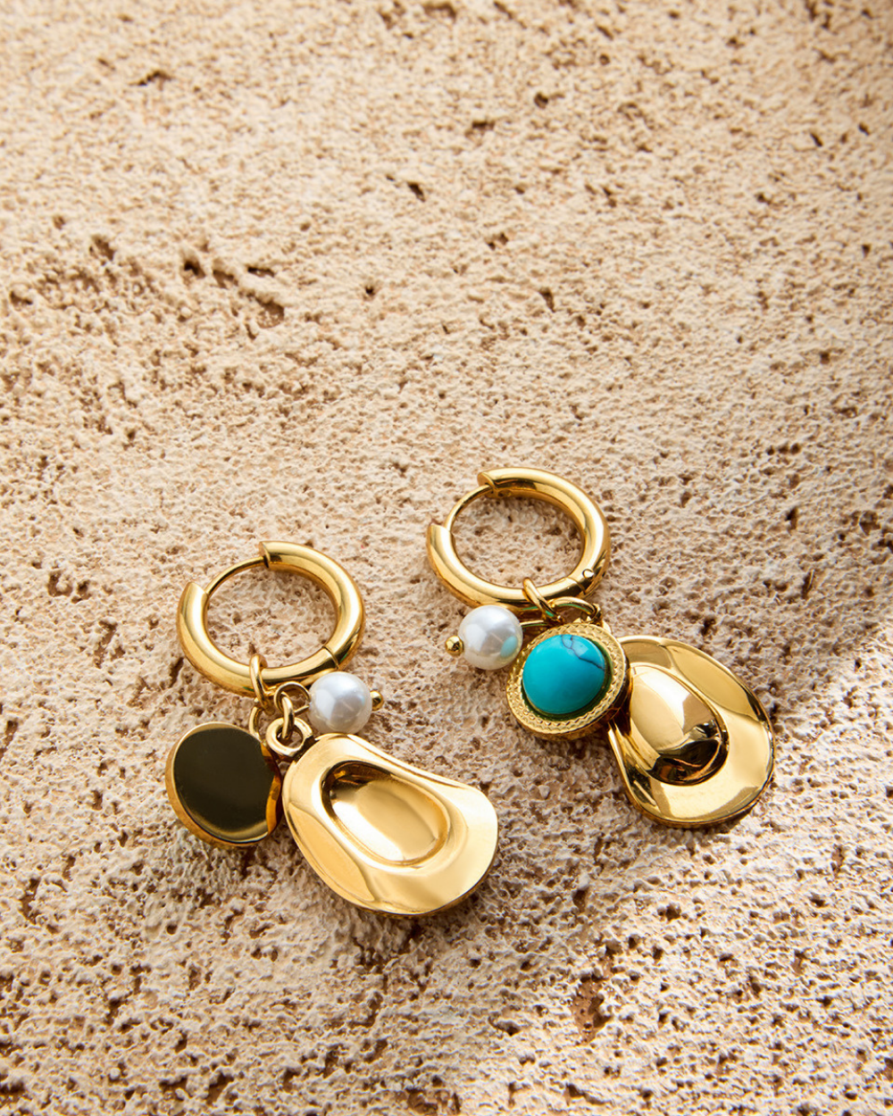 Gold earrings with various charms on a textured beige surface