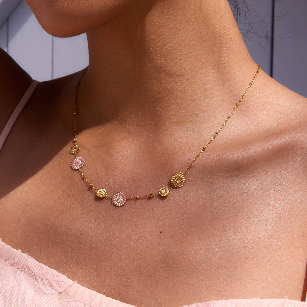 Model wearing layered daisy necklace under straw hat in soft sunlight