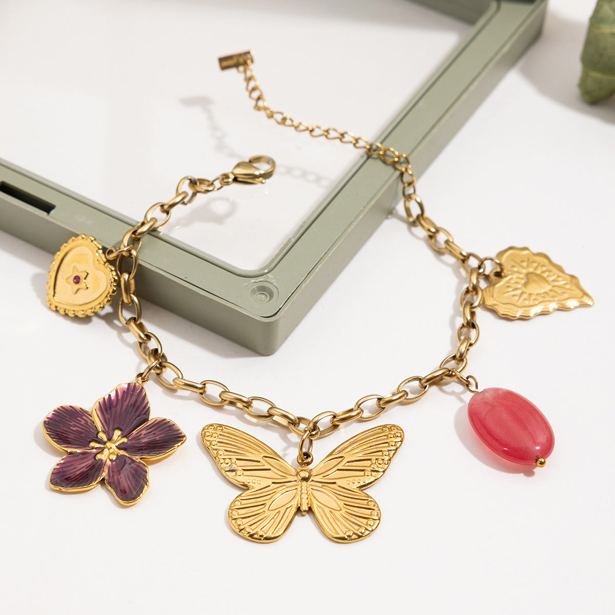 Hand holding charm bracelet with pink bead and gold detailing
