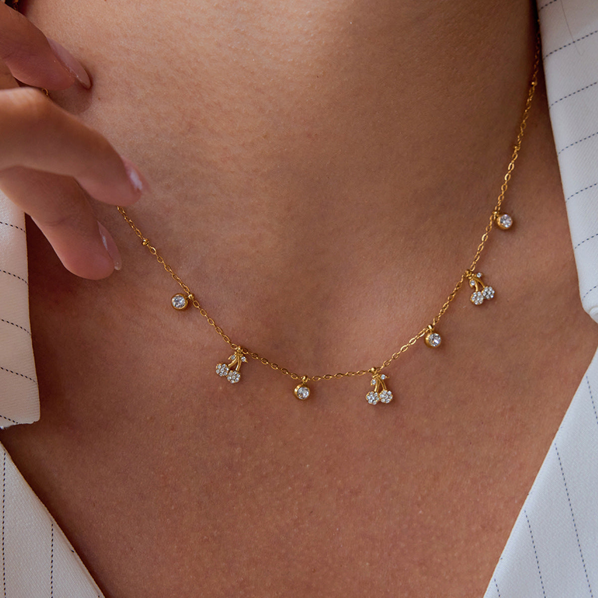 Model wearing gold cherry charm necklace with white striped outfit, close neck view