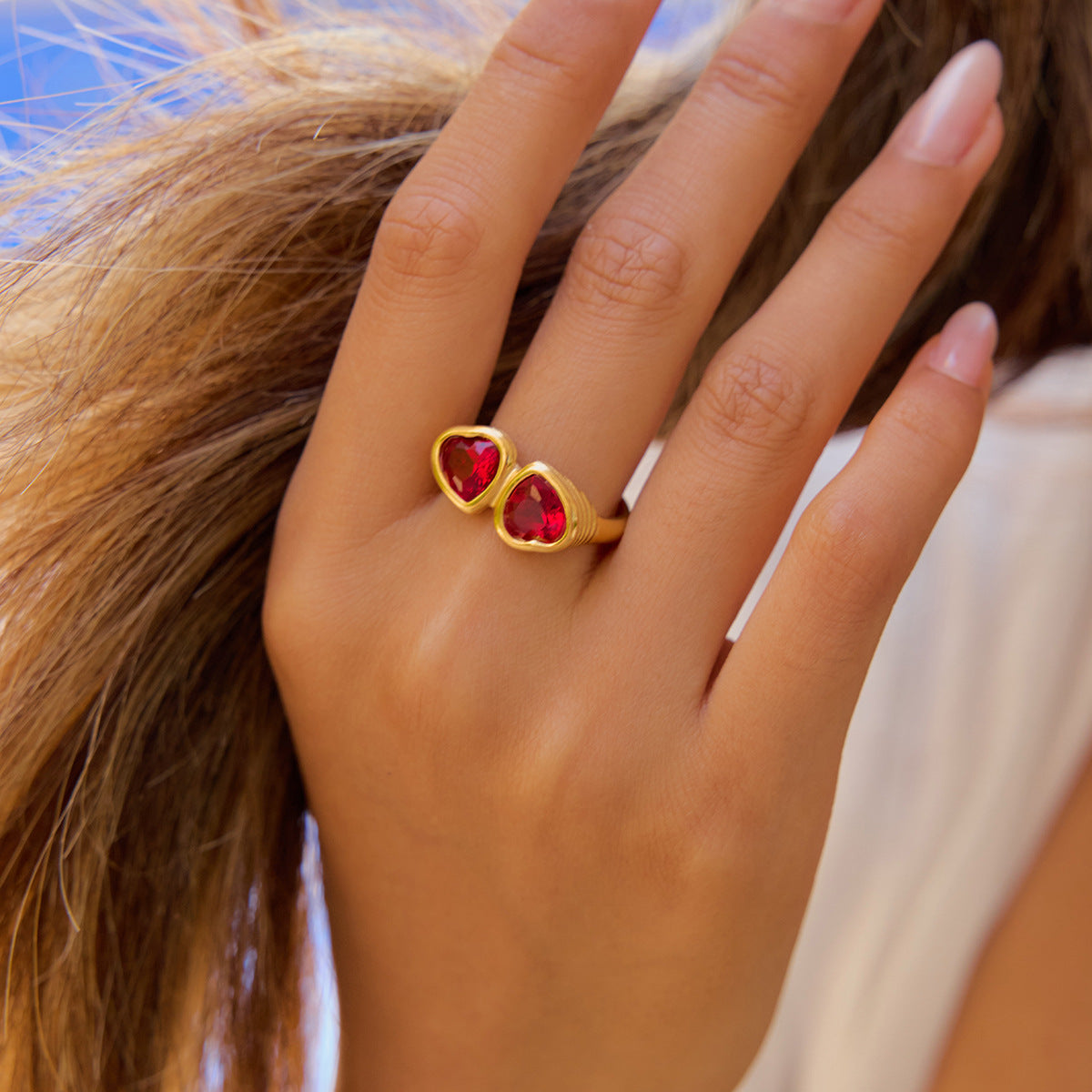 Hand brushing hair with gold heart ring sparkling under natural sun