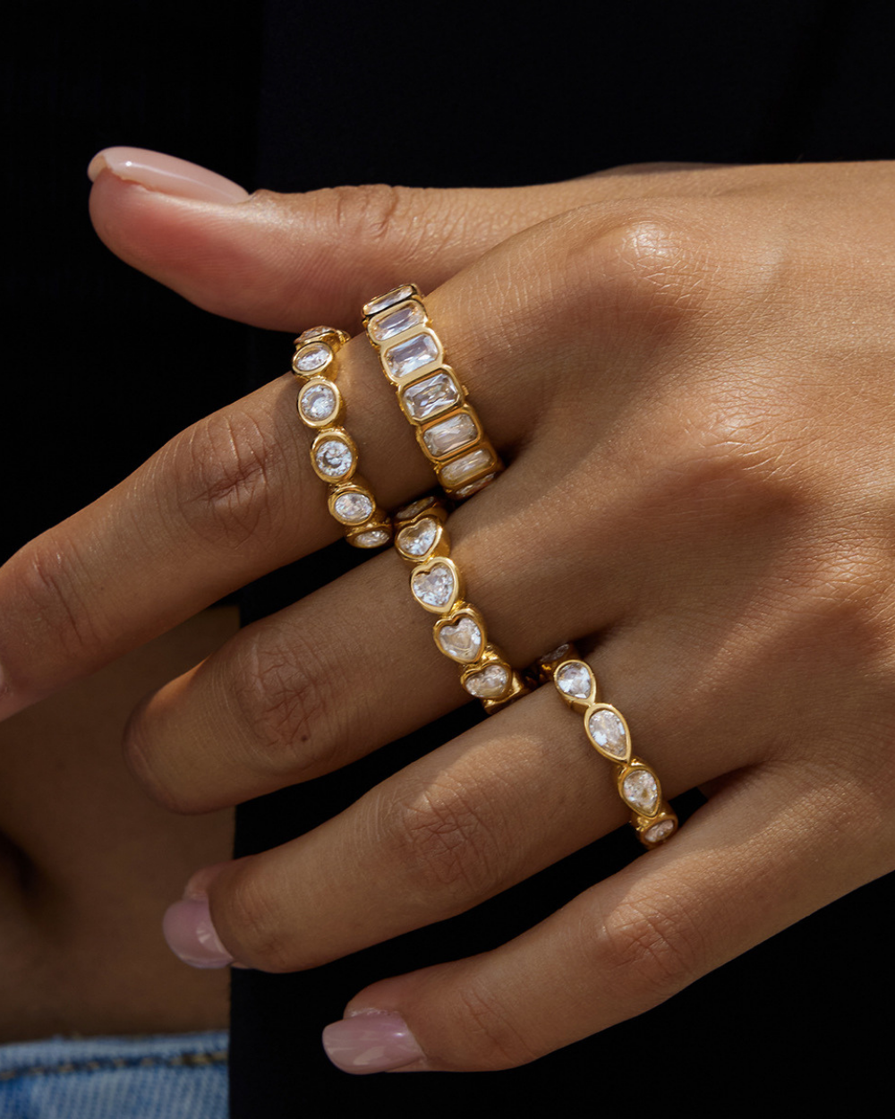 Gold rings with gemstones on a hand against a black background