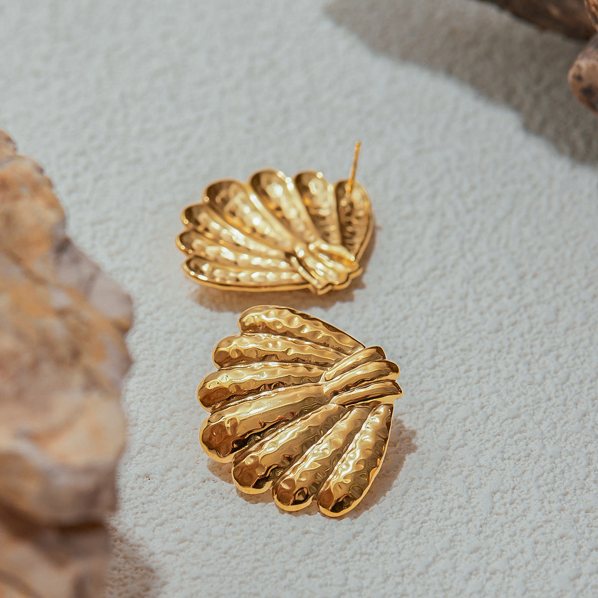 Flatlay of hammered seashell earrings on sand-colored surface with rocks