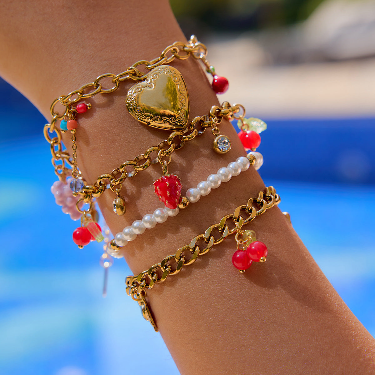 Layered gold bracelets including berry charm bracelet worn by model poolside in summer