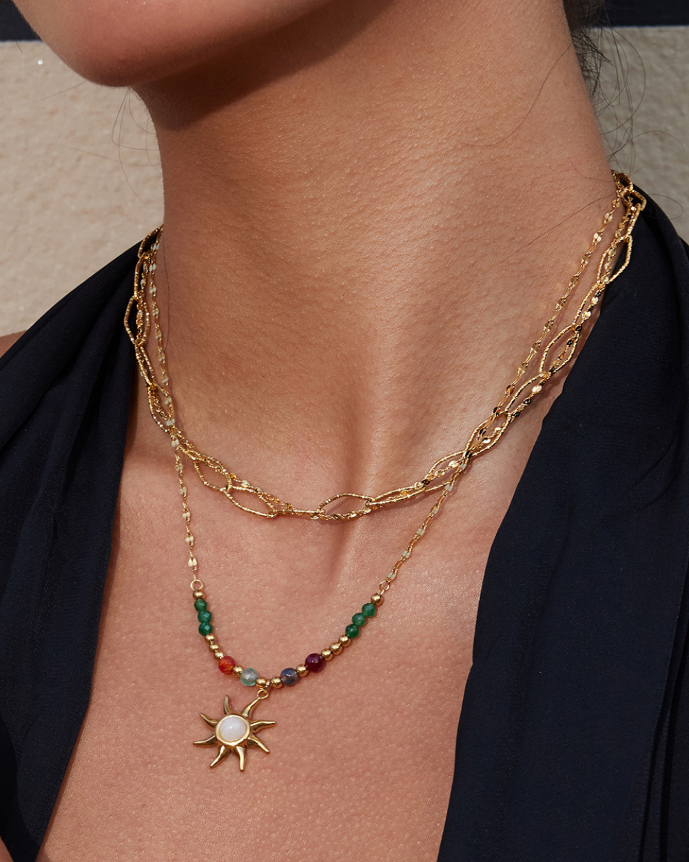 Close-up of a person wearing a gold necklace with a sun pendant and colorful beads.