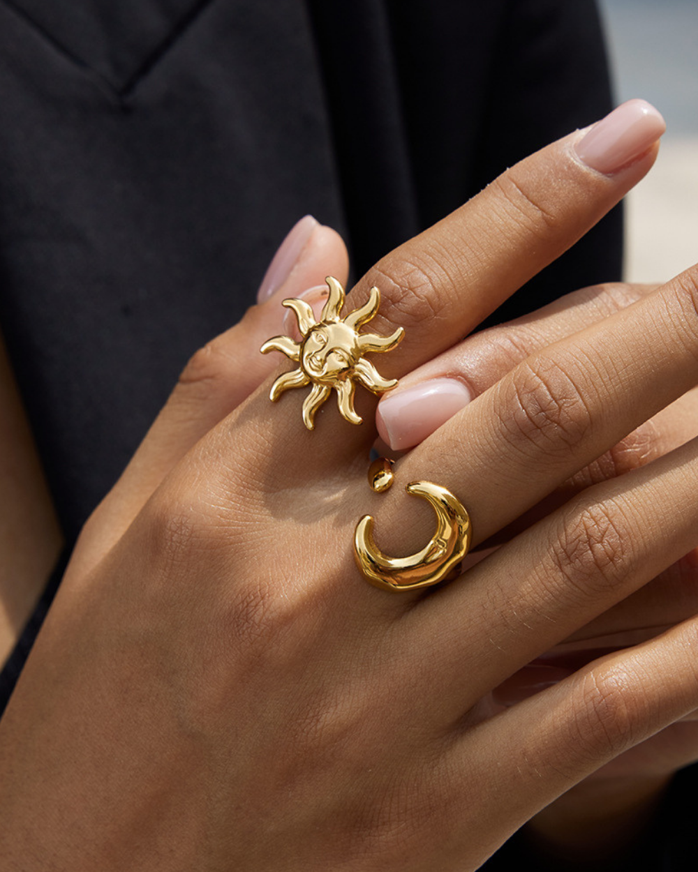Gold sun and moon ring on a hand against a dark background
