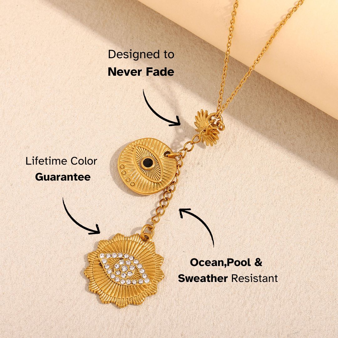 Gold necklace with engraved eye and sunburst pendants, laid on soft fabric, featuring protective symbolism.