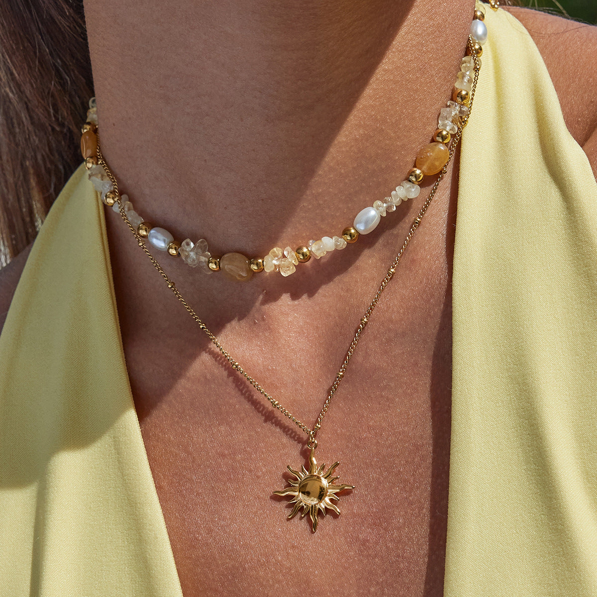 Gold necklace with sun pendant worn by a person in a yellow top.