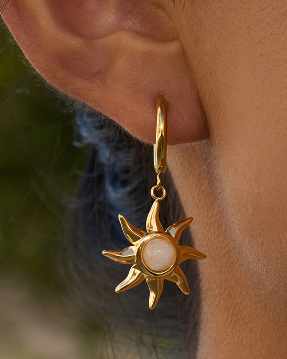 Gold sun-shaped earring with a pearl center worn by a person.