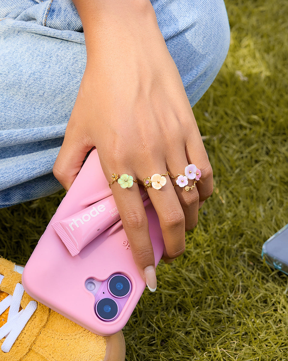 Person holding a pink phone case with floral ring designs on a grassy background