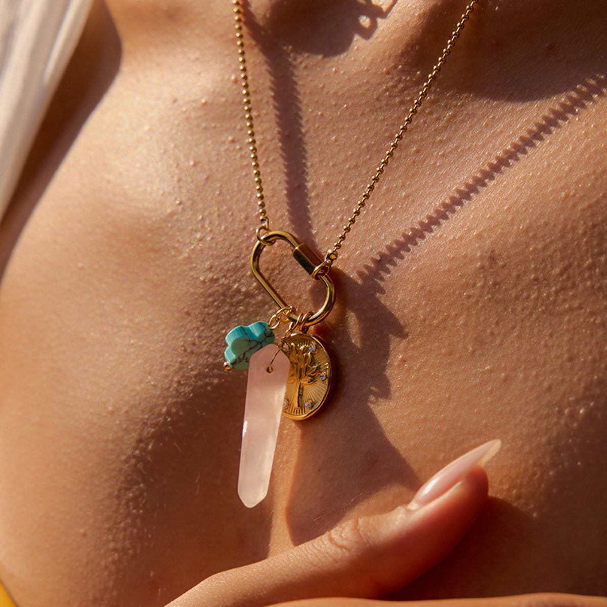Model layering crystal charm necklace with gold chain under sunlight