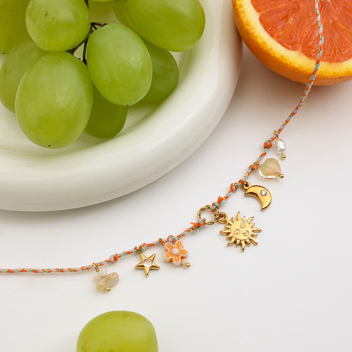 Close-up of charm necklace with sun, moon, and star pendants styled on white plate with grapes and orange