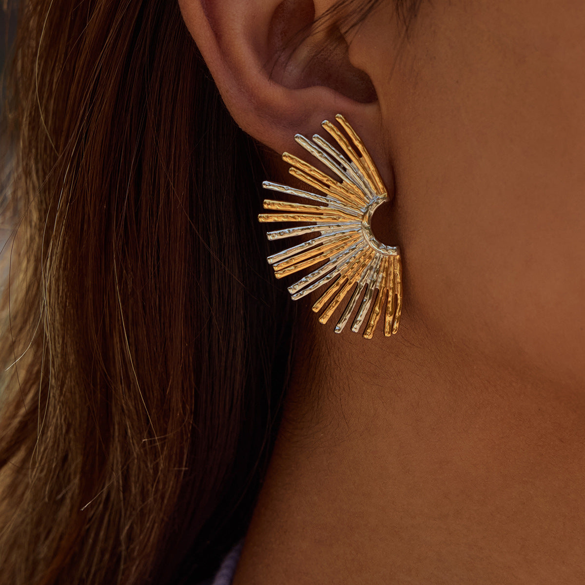 Large gold and silver sun-inspired earrings worn by model, hair tucked back