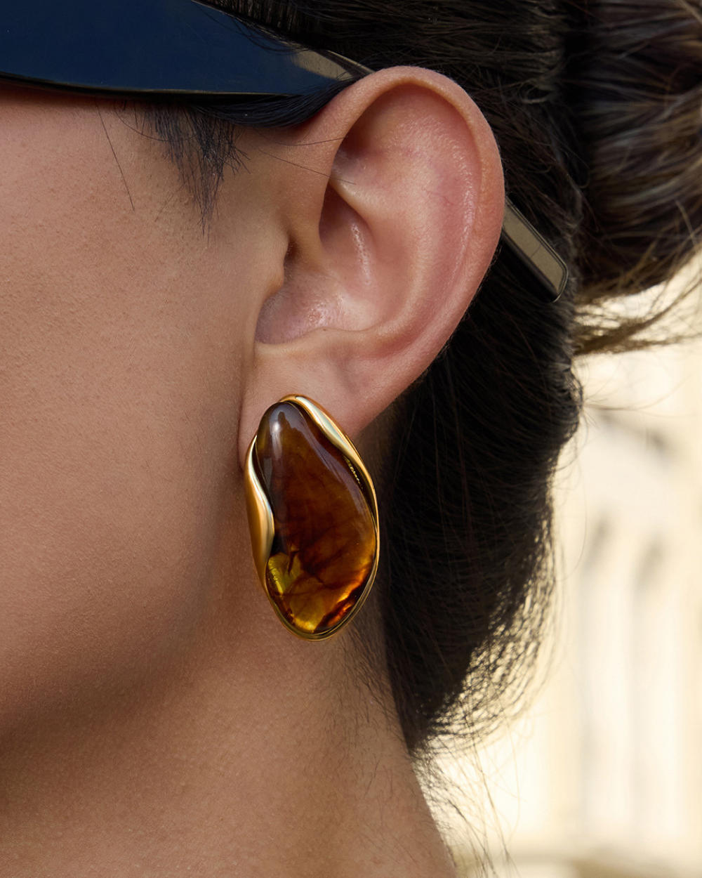 Close-up of an ear wearing a gold and amber earring with blurred background