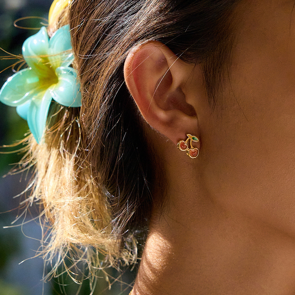 Close-up of an ear with cherry-shaped earrings, hair with a flower accessory.