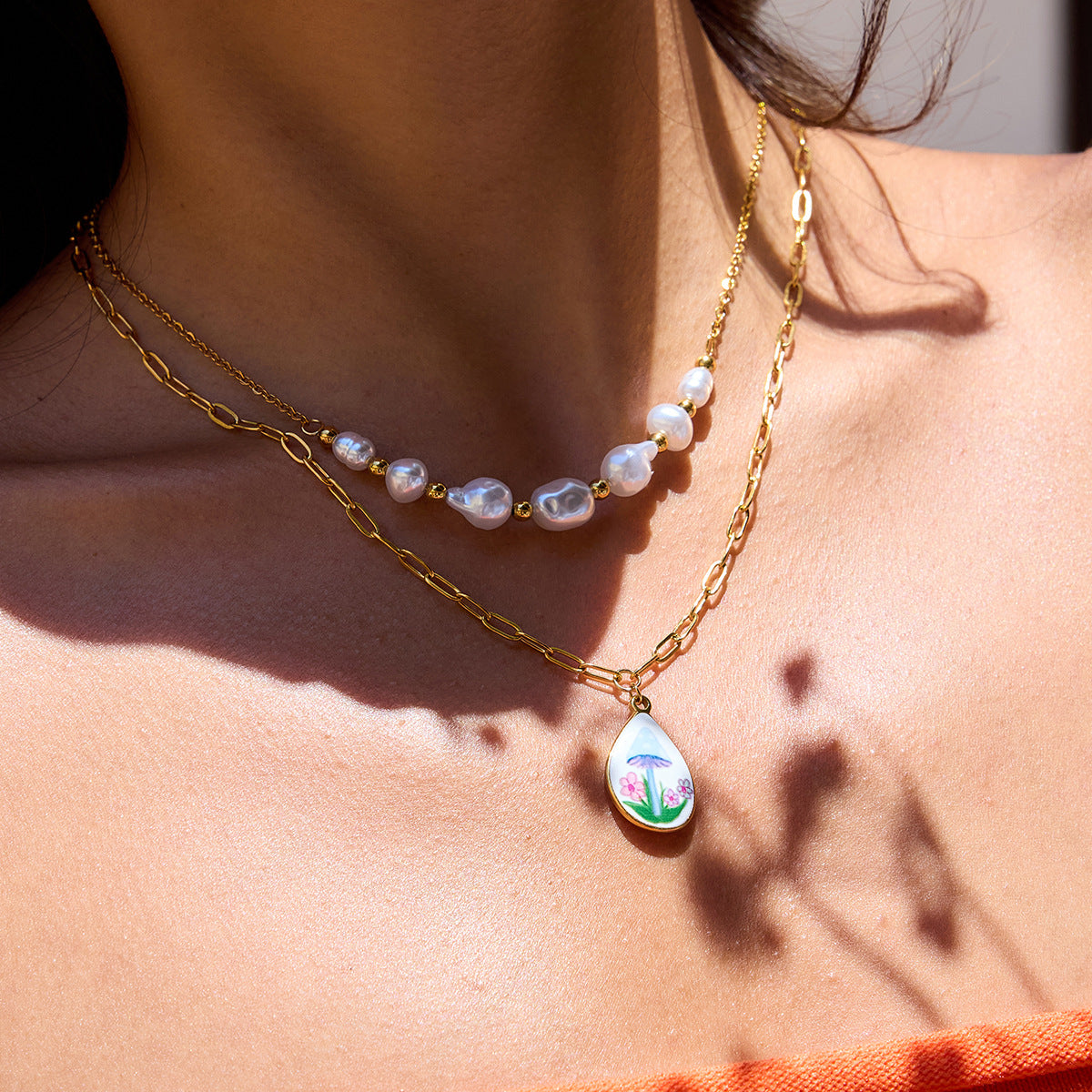 Model wearing gold and pearl layered necklace with floral mushroom enamel charm in orange top