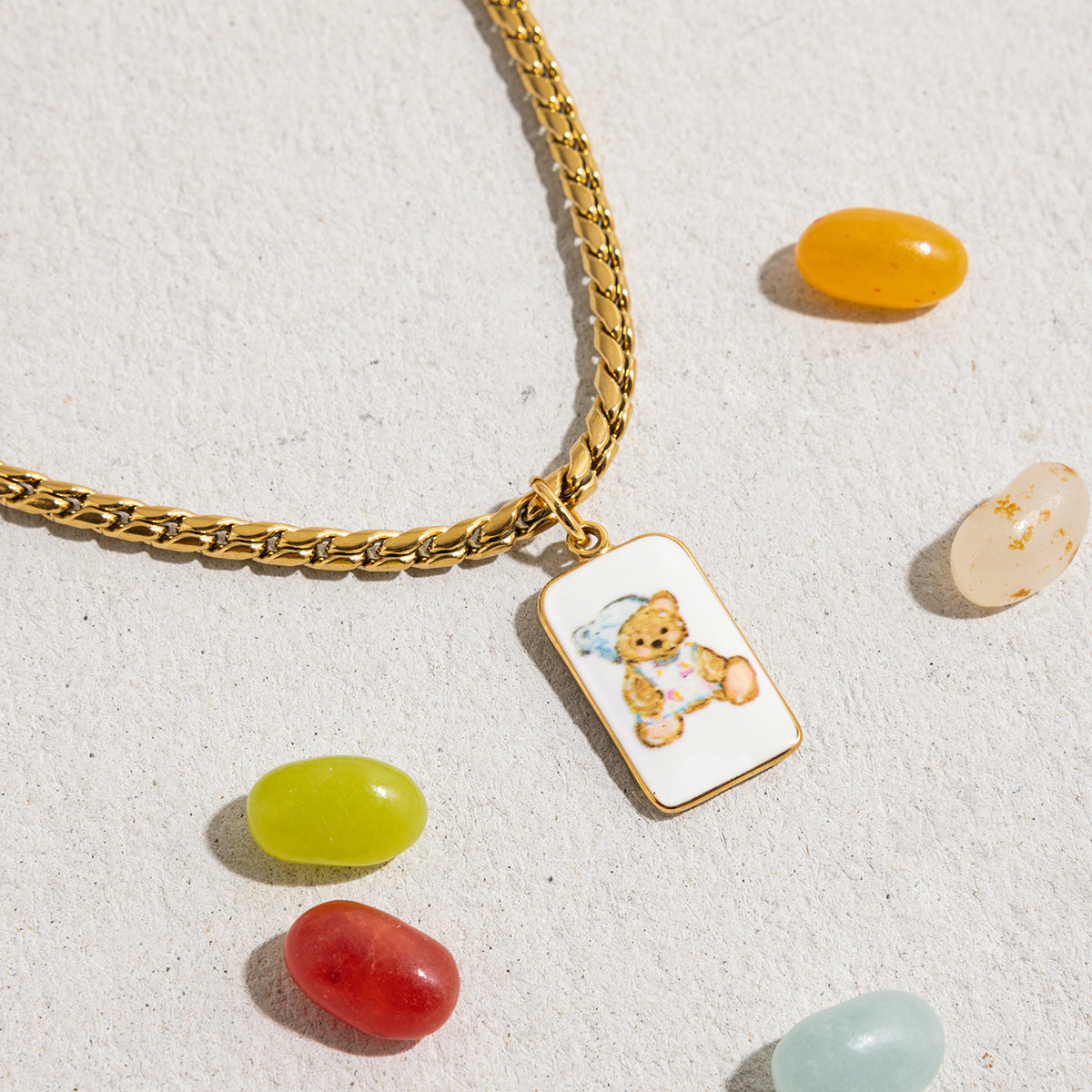 Bear charm necklace styled with candy elements on textured concrete background