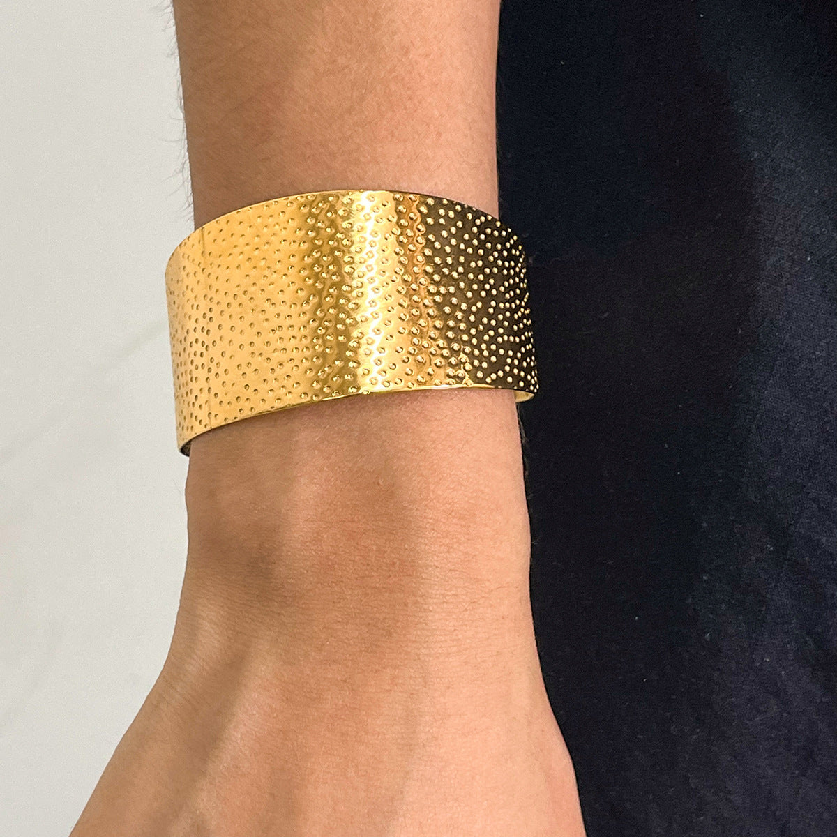 Gold textured cuff bracelet on a wrist with a neutral background