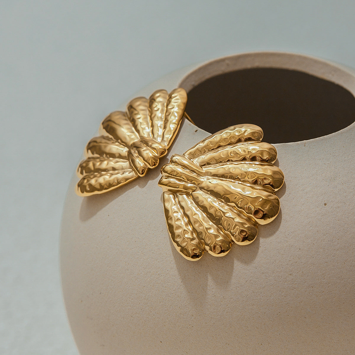 Pair of gold hammered seashell earrings resting on ceramic vase