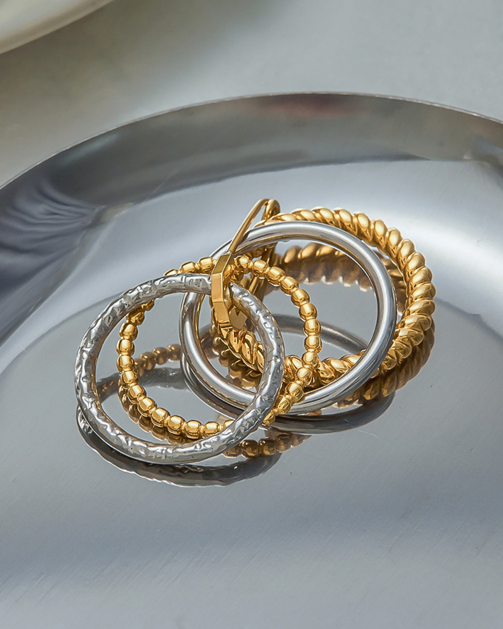 Gold and silver hoop earrings on a reflective surface