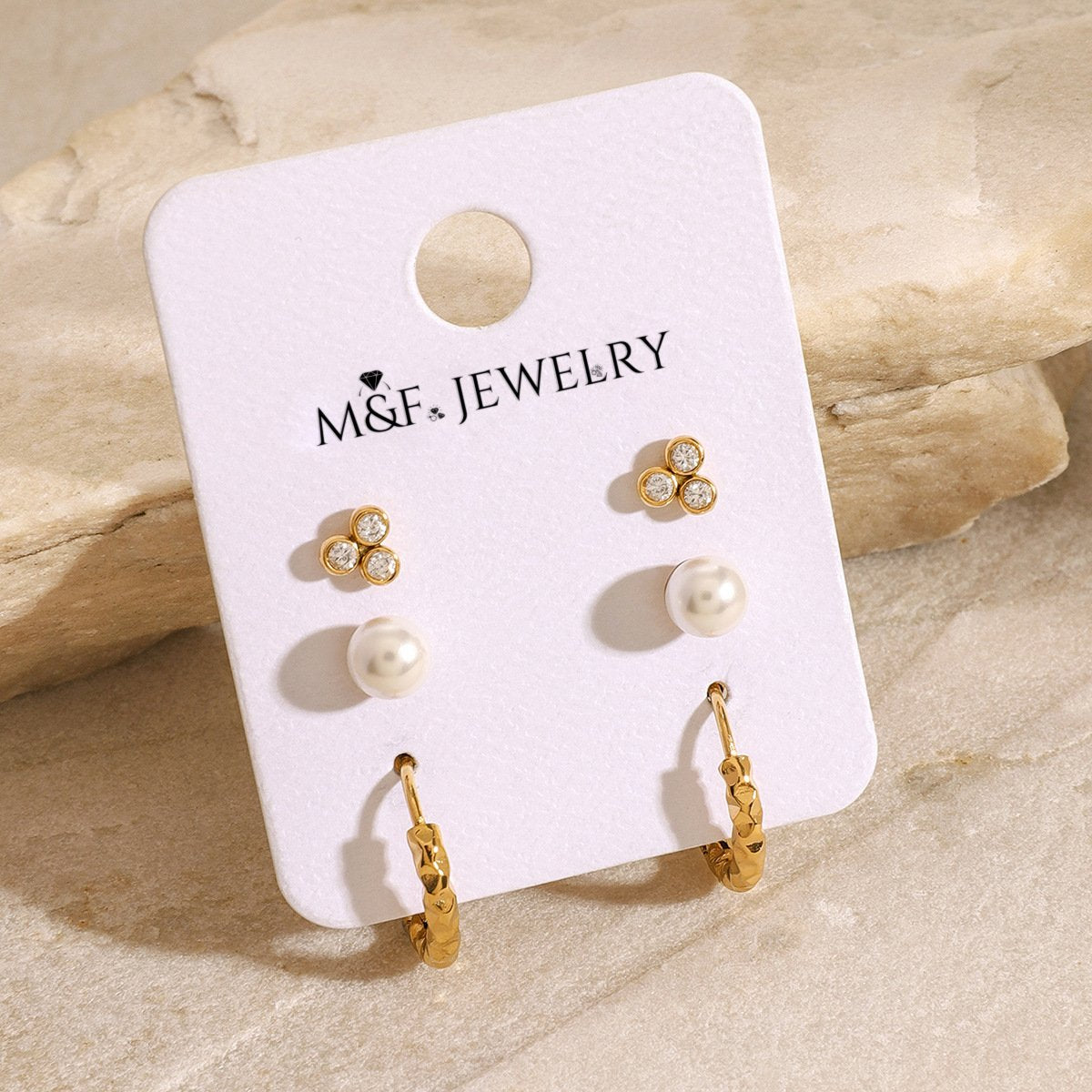 Trio of gold earrings including hammered hoops, pearl studs, and crystal clusters on display card