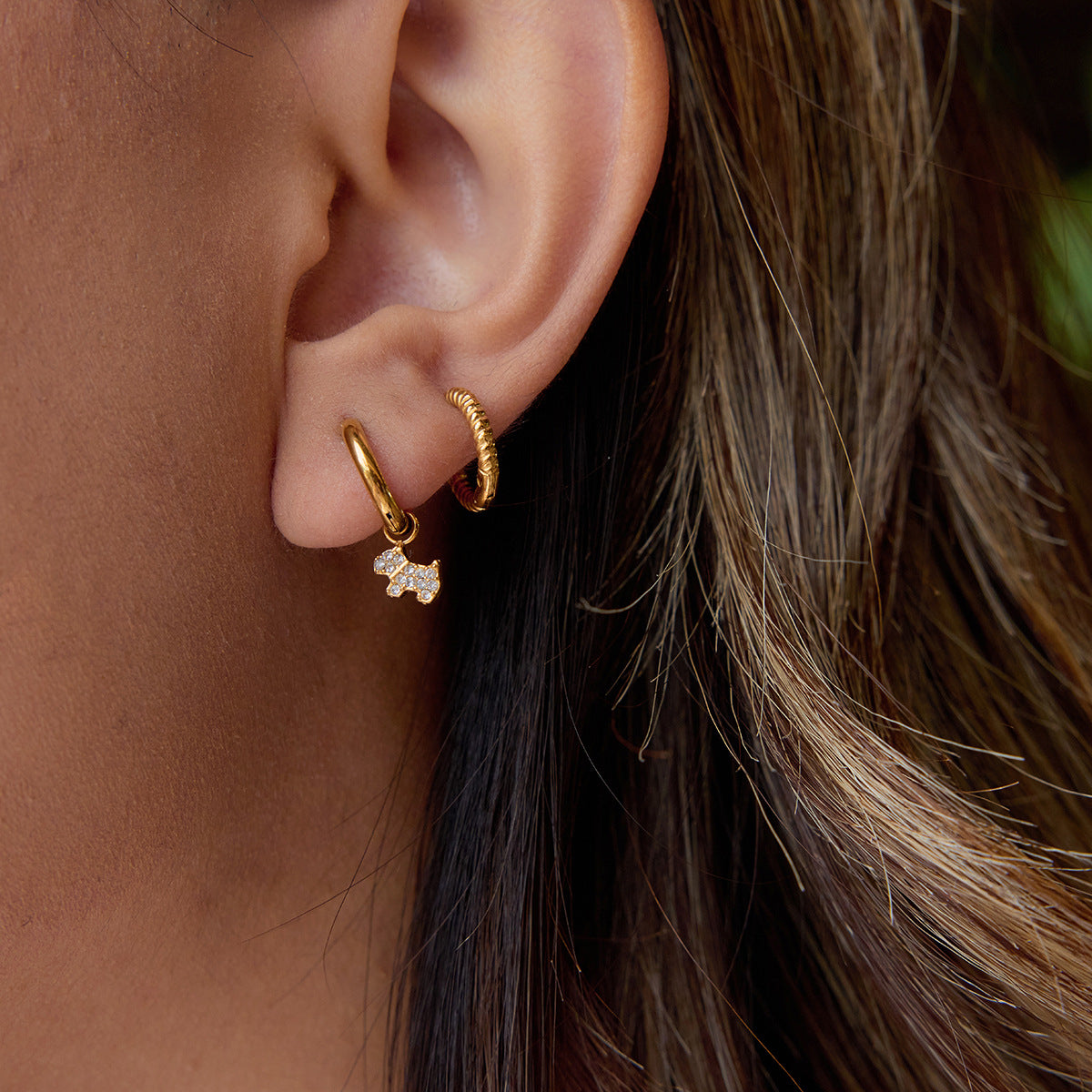 Close-up of gold huggie earrings with sparkly dog charm worn by woman with brown hair