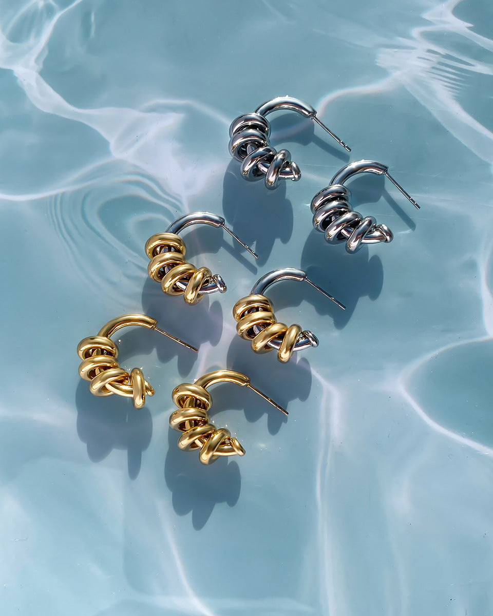 Set of spiral-shaped earrings in gold and silver on a light blue water-like background
