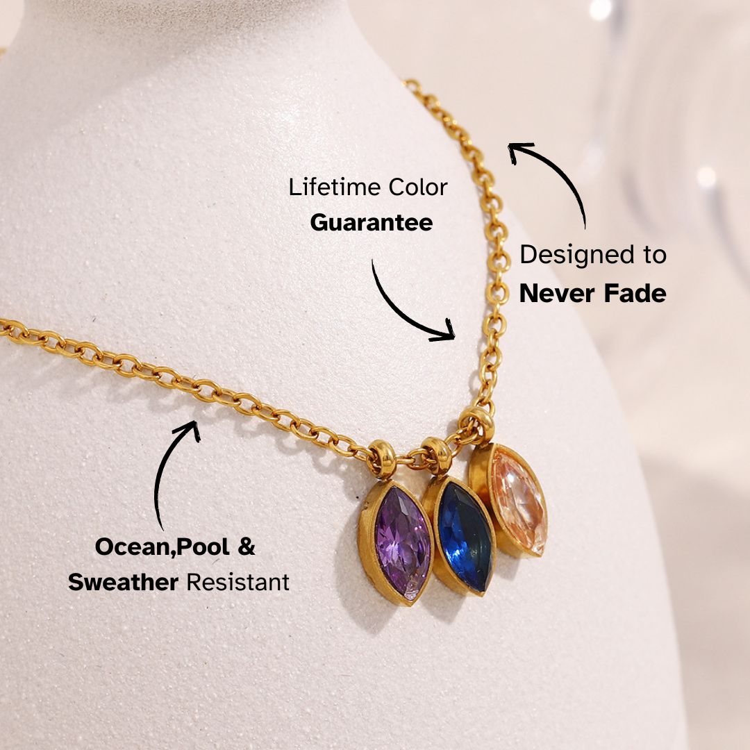 Minimal gold chain necklace with three teardrop-shaped gems in purple, blue, and peach, styled on mannequin.