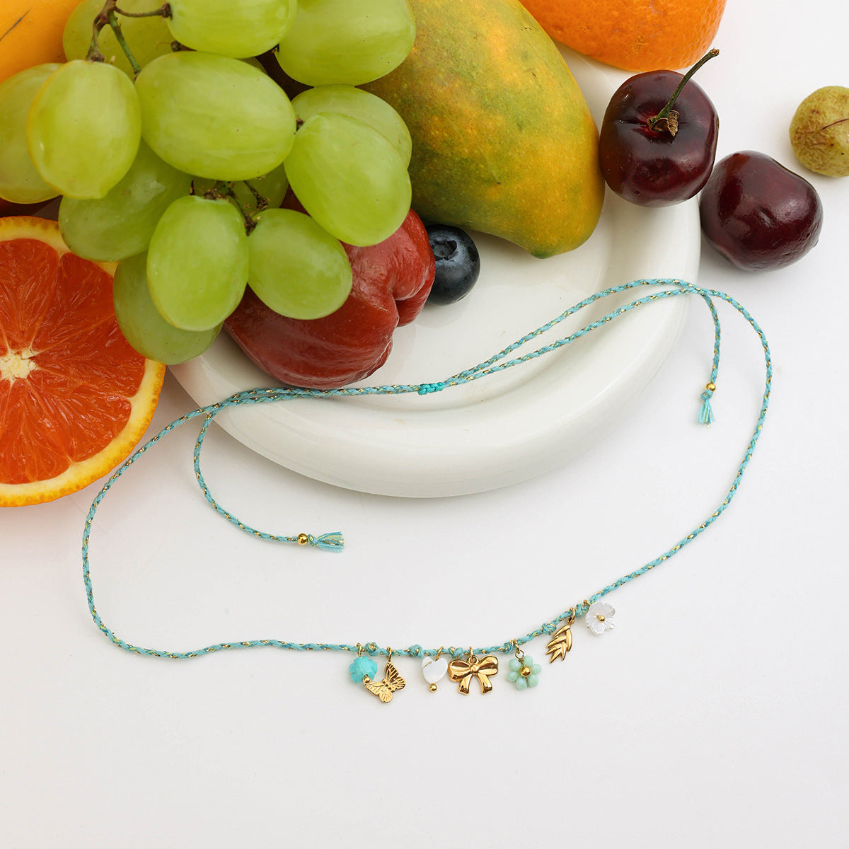 Boho-inspired necklace with colorful resin flowers and butterfly charms, flat lay with fruit