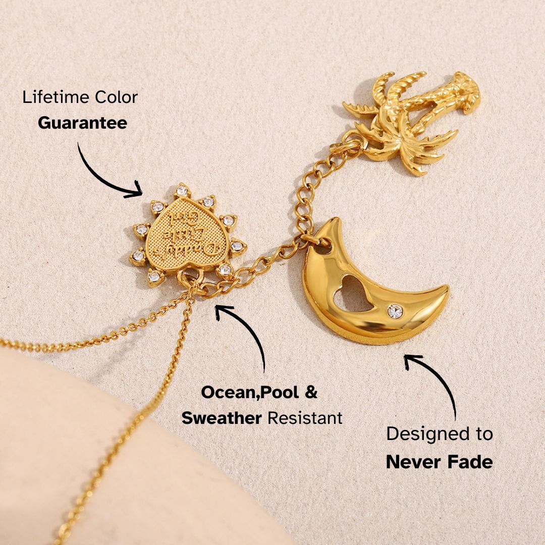 Boho gold necklace with palm tree and moon charms, laid on sand background, ideal for vacation styling.