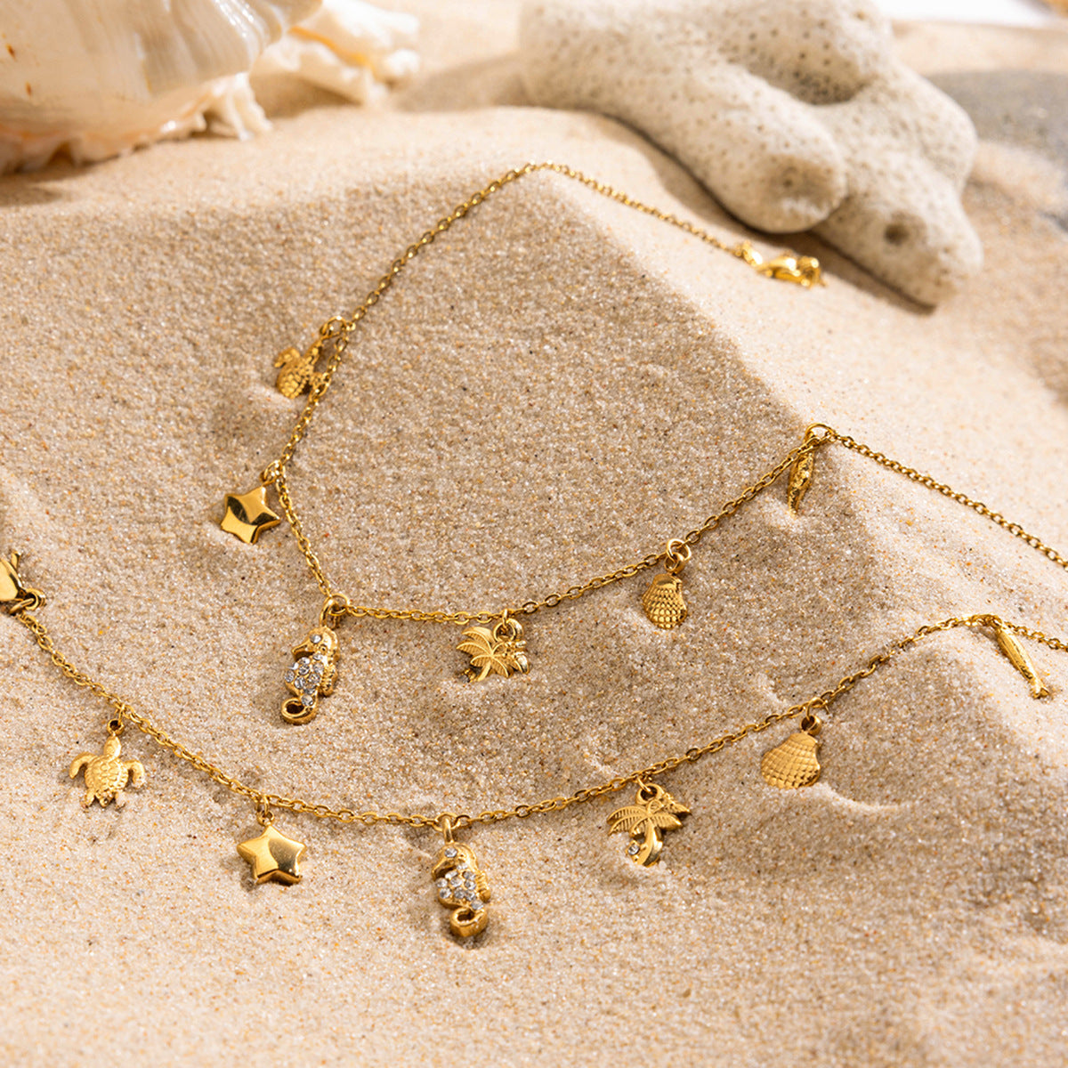 Gold charm necklace with seahorse and palm pendants styled on beach sand with stone