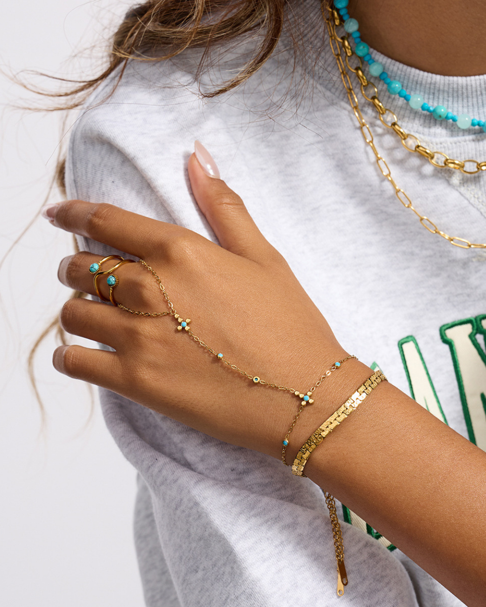 Hand wearing gold bracelets with turquoise stones on a white background