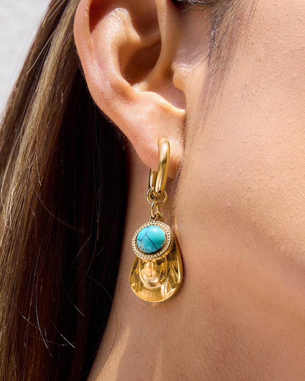 Gold earring with turquoise stone worn by a person