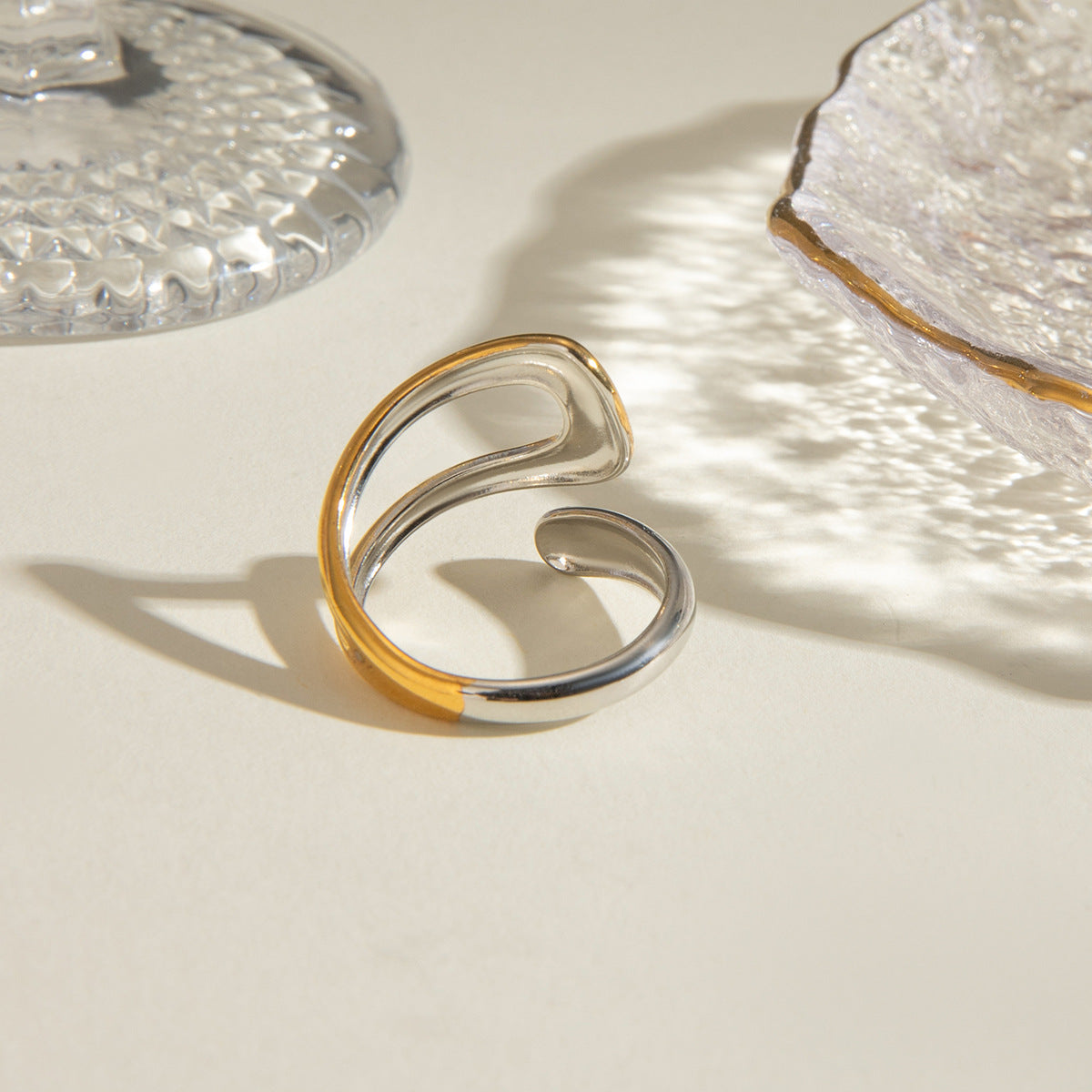 Curved open band ring in gold and silver tones, minimalist style on tabletop.